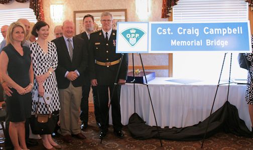 OPP commissioner Vince Hawkes (R) poses for a photo with the Campbell family beside the sign in honour of OPP constable Craig Campbell